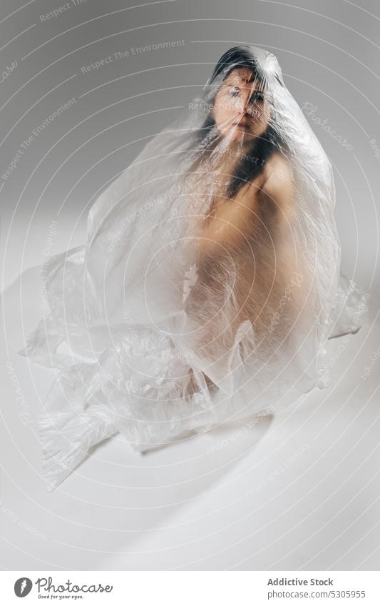 Woman wrapped in polyethylene sitting on floor woman naked nude pollute disaster environment ecology rubbish cellophane female helpless concept cover damage