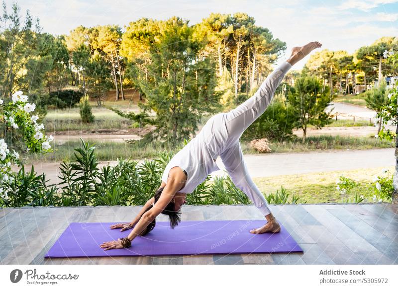 Concentrated woman practicing yoga on mat near park asana standing splits urdhva prasarita eka padasana flexible meditate stretch practice tropical balance