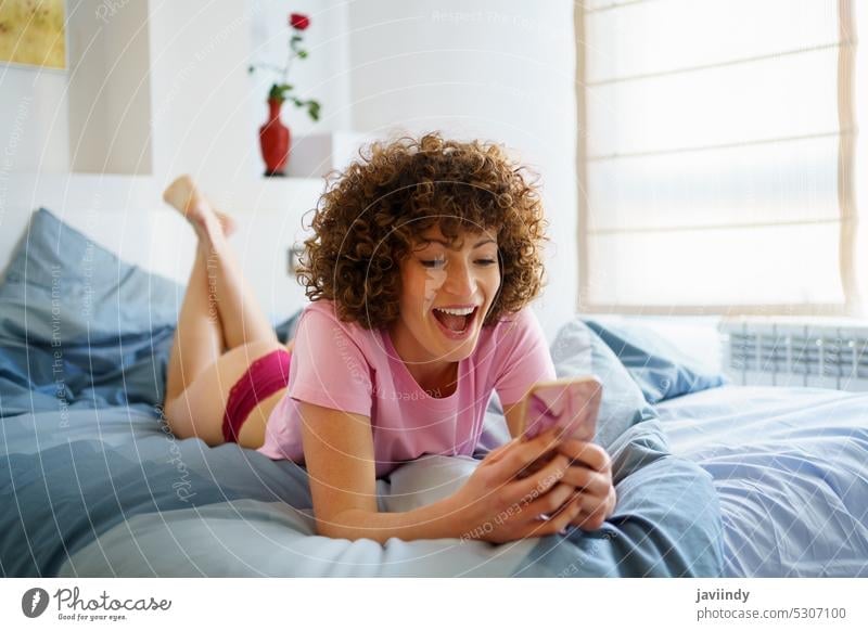 Excited woman using cellphone while lying in bed at home smartphone amazed excited watch video browsing comfort bedroom female gadget device mobile young relax