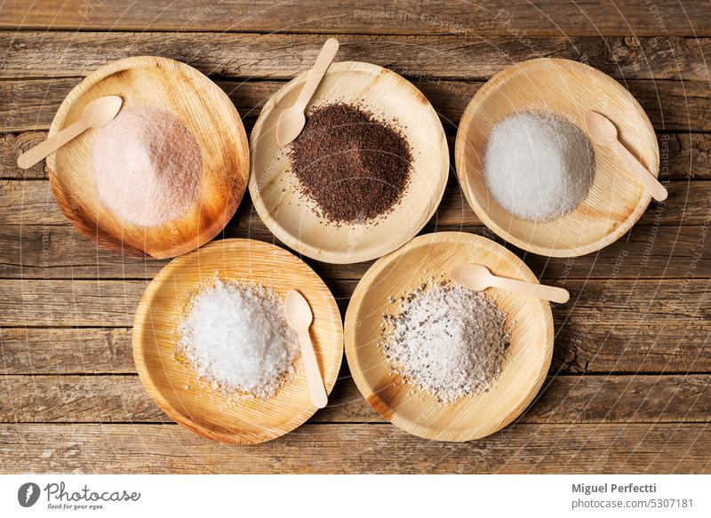 Wooden plates with different types of salt, pink, black, marine or normal, flakes and seasoned with truffle, on a rustic wooden table. Top view. condiment