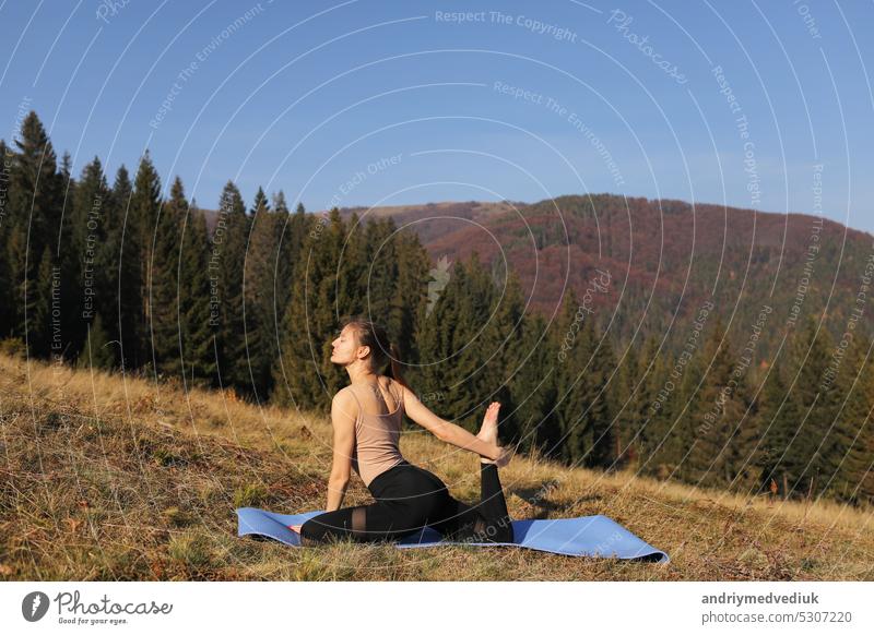 Young fit woman doing exercises on yoga mat on background of sunny mountains hills. Outdoor workout, healthy lifestyle. female in sport suit is stretching in nature against the forest in the morning