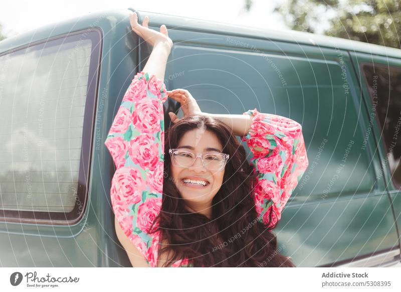 Smiling woman standing against olive green colored car sunlight summer glad eyeglasses cheerful smile optimist content carefree happy joy young freedom female