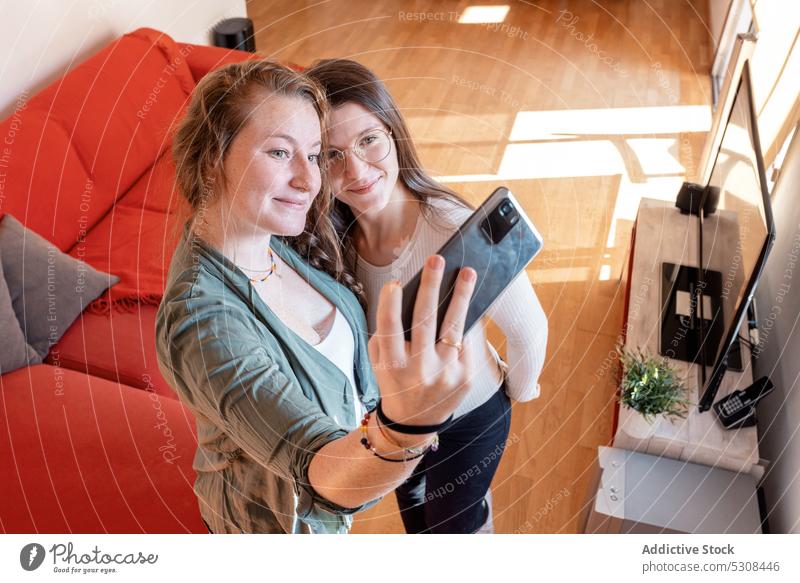Smiling women standing and taking selfie on smartphone at home friend positive smile together cheerful using window mobile happy gadget device young female