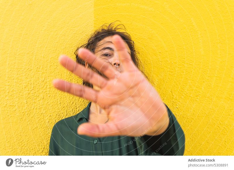 Calm woman hiding face behind hand on yellow background reach out cover face serious confident hide gesture street trendy appearance young female casual style