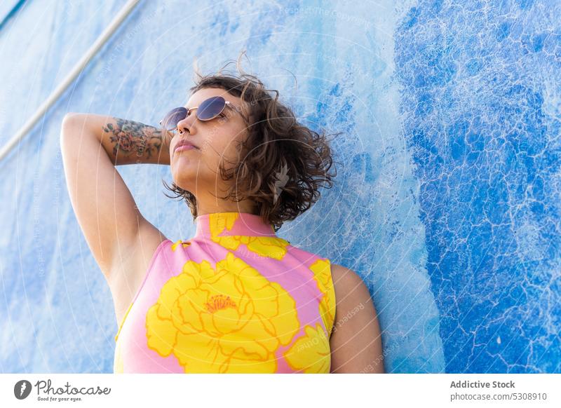 Pensive woman in sunglasses looking away on street summer style short hair colorful urban modern fashion wall female trendy confident curly hair individuality