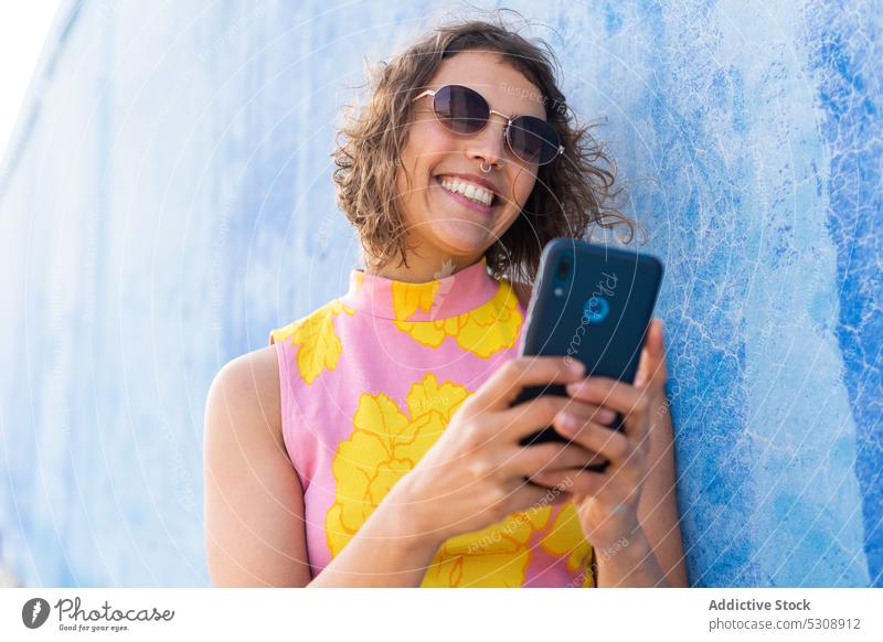 Cheerful woman browsing smartphone on street using message smile colorful happy summer style cheerful female sunglasses curly hair young mobile wall trendy
