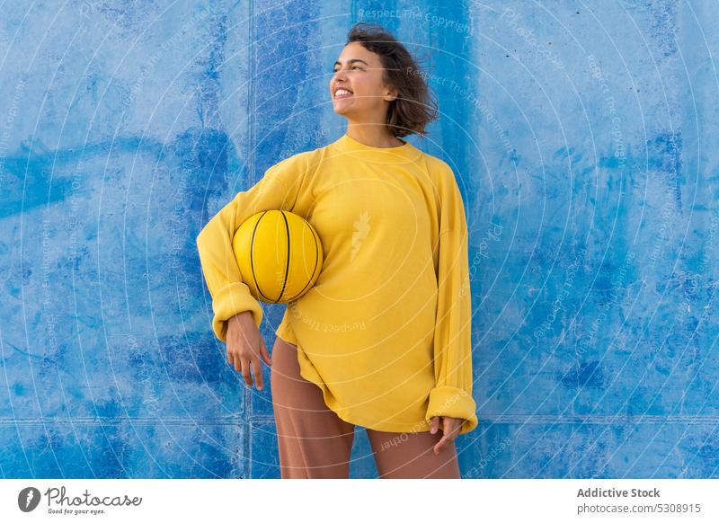 Positive woman playing with ball against blue wall throw basketball cheerful sports ground smile happy game young player training active activity positive