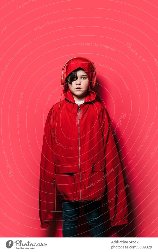 Young girl in oversized hooded raincoat outfit in studio casual childhood kid headphones confident headset colorful modern serious hoodie little young cool