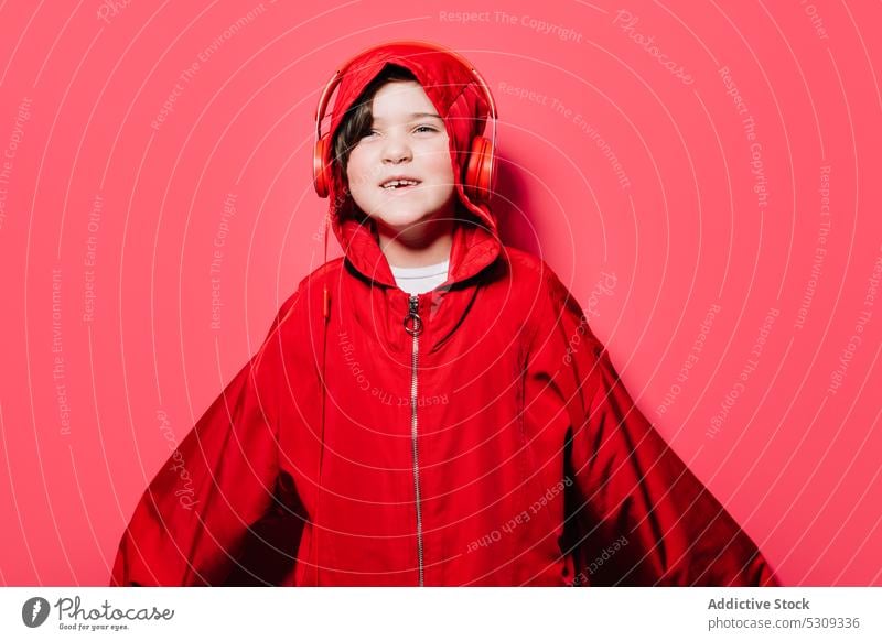 Happy young girl in oversized hooded raincoat outfit in studio casual childhood kid headphones confident headset colorful smile modern delight hoodie glad