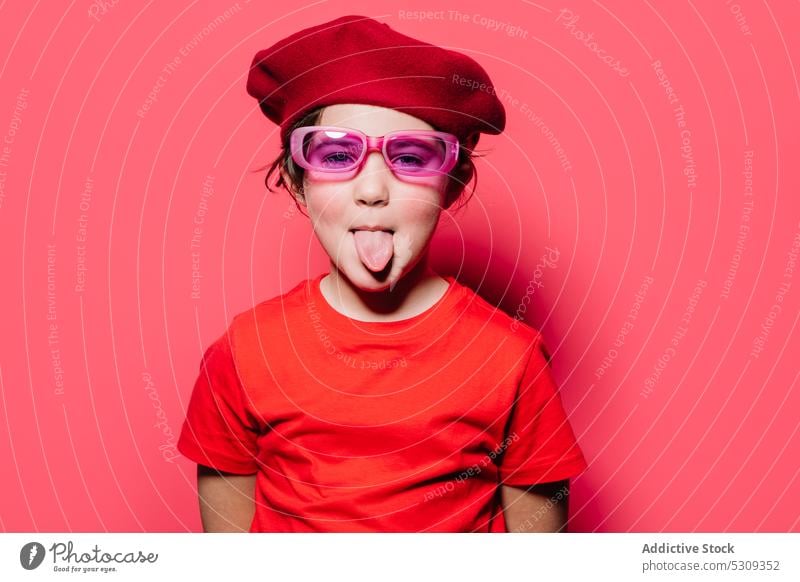 Funny kid in red casual outfit with glasses and beret style mouth opened show tongue make face humor funny girl model child fashion vivid colorful tongue out