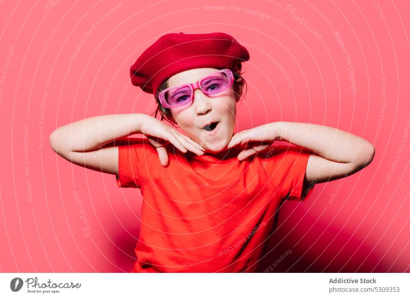 Funny girl in red casual shirt and beret making superhero pose while looking at camera style surprise kid trendy outfit fashion expressive mouth opened amazed