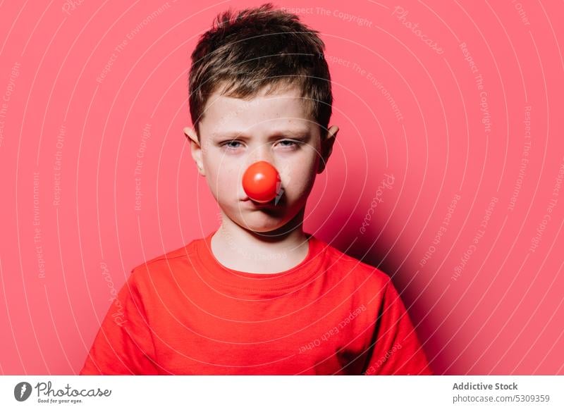 Sad boy in red nose looking at camera kid portrait clown sad calm casual unhappy child adorable cute t shirt young childhood individuality color male headshot