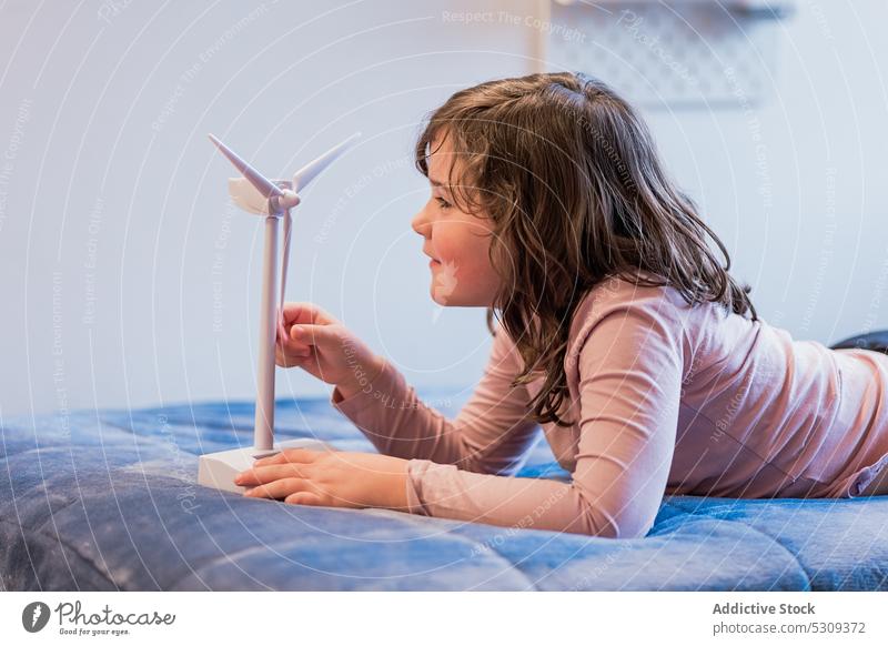 Girl playing with mockup of wind turbine on bed girl kid child having fun bedroom childhood happy smile joy positive lying comfort home dream cute soft adorable