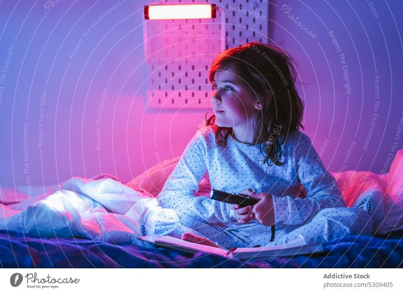 Adorable girl using flashlight on bed at night book curious legs crossed bedroom story child interest illuminate read fairytale cute pajama childhood fiction