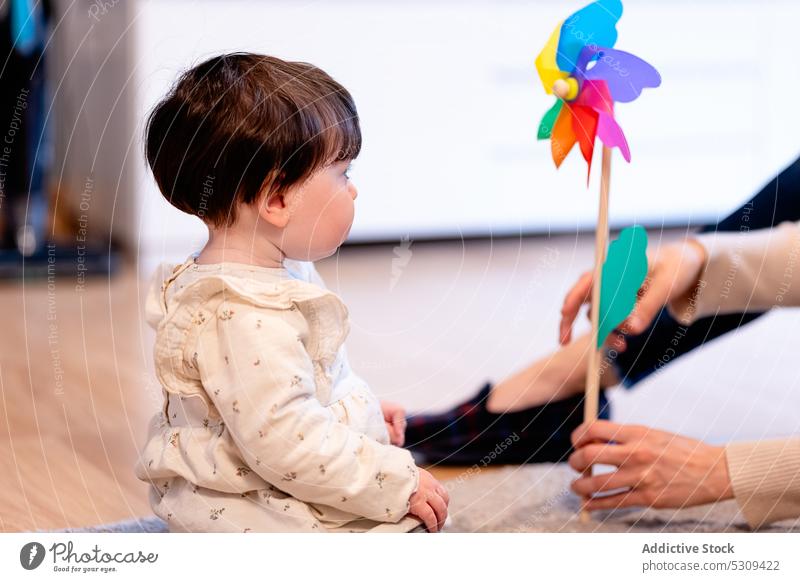 Crop mother holding pinwheel while playing with daughter baby toy cute together little colorful girl child love motherhood curious childhood kid adorable home