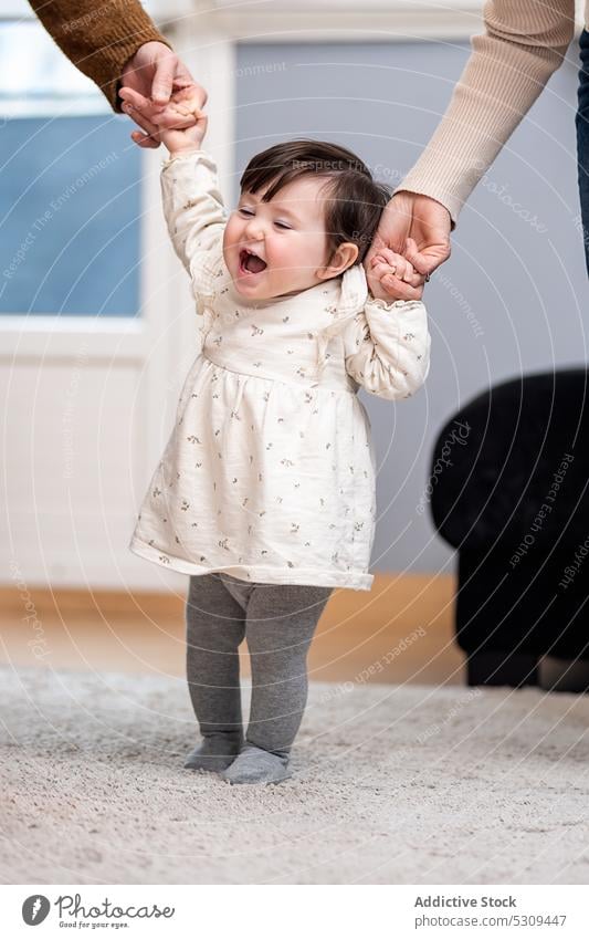 Cute little baby learning to walk with parents at home family daughter holding hands support trust cute adorable innocent together relationship child father