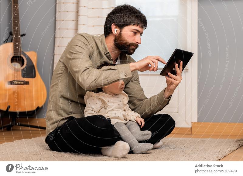 Curious girl looking at screen of tablet near man sitting on floor father daughter using remote home work browsing freelance kid child gadget connection device