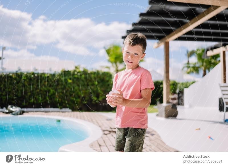 Cute boy with balloon in backyard near swimming pool summer resort holiday sun kid vacation child adorable childhood cute water joy poolside casual recreation