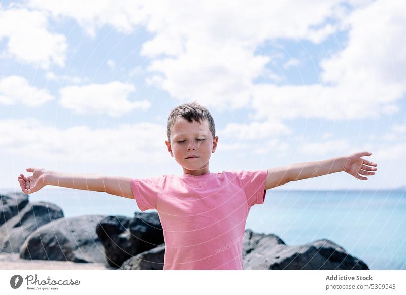 Relaxed boy standing near sea with eyes closed meditate stone calm yoga balance seaside child rock male beach practice harmony ocean young nature relax spirit