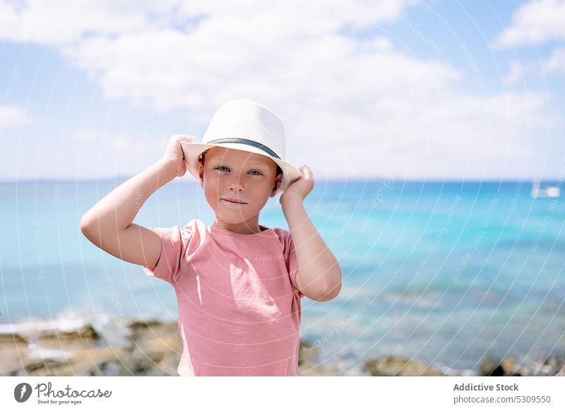 Boy in hat standing near sea in daylight boy blue sky summer confident child nature ocean kid young childhood lifestyle beach carefree outside summertime