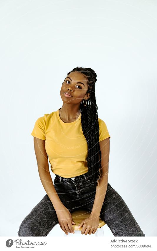 Smiling black woman sitting on chair against white wall smile positive trendy braid content appearance style confident female young casual ethnic calm