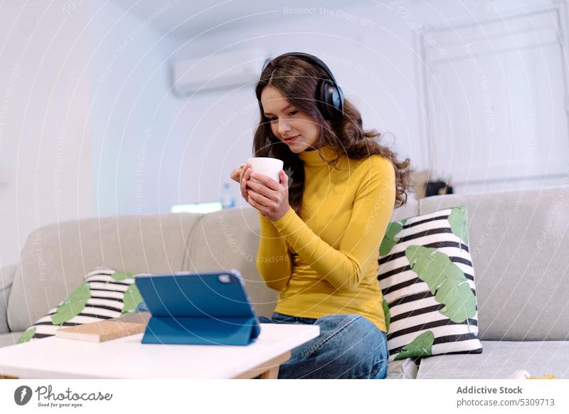 Calm woman with tablet listening to music in headphones on sofa smile home using positive browsing online internet female young happy surfing device
