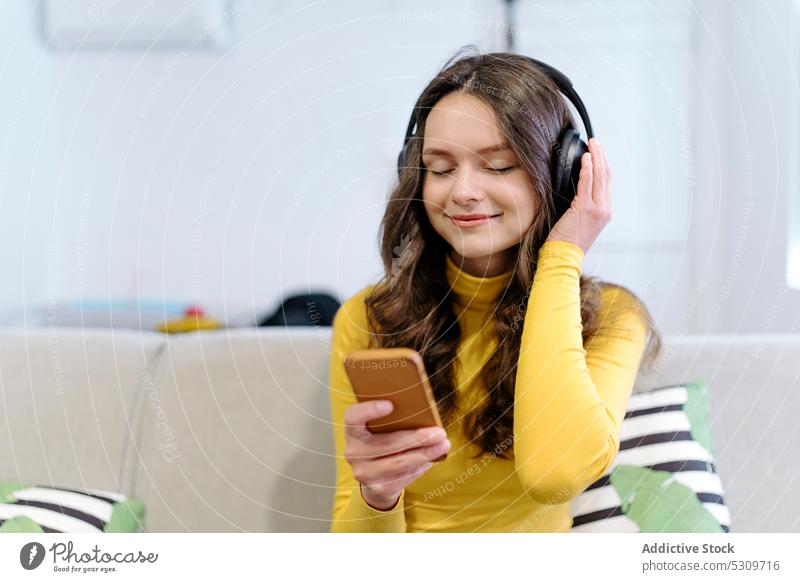 Calm woman with smartphone listening to music in headphones on sofa smile home eyes closed positive female young happy cheerful device casual gadget meloman