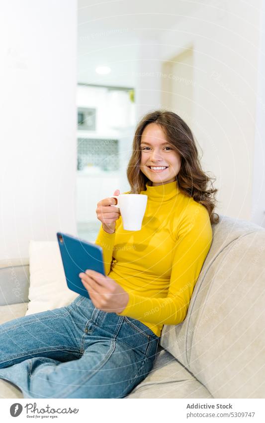 Focused happy woman with coffee browsing tablet on sofa using smile concentrate drink online home delight living room surfing internet gadget glad device focus