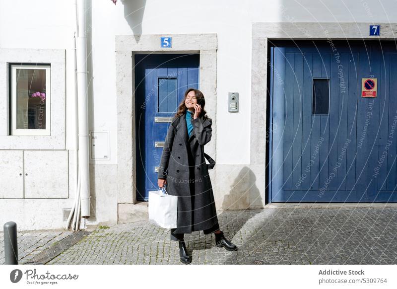 Cheerful woman with shopping bag on street entrance smile happy pavement door building urban shopper female young eyes closed cheerful doorway style positive