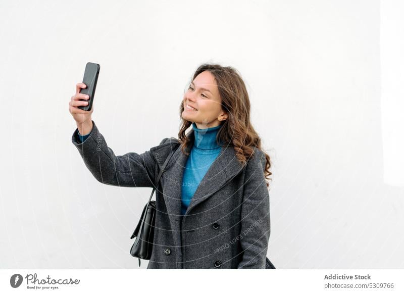 Smiling woman taking selfie on smartphone on white background using self portrait smile cheerful bag happy coat gadget device mobile cellphone female