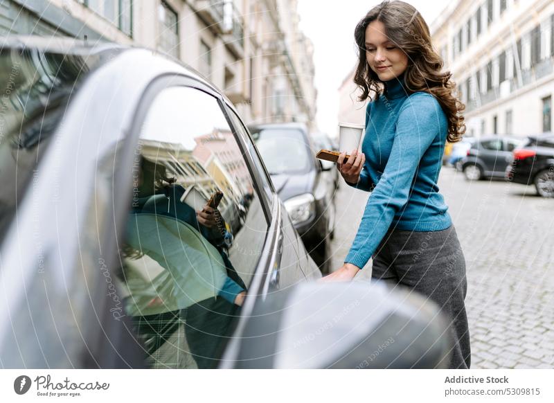 Woman with smartphone standing near car on street woman smile positive coffee city automobile vehicle transport to go takeaway disposable open door toothy smile