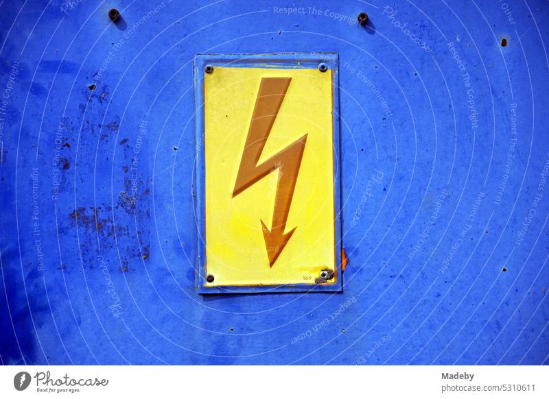 Red lightning on yellow background warning of high voltage on a rusty blue old junction box at the marina on the Moselle river in Traben-Trarbach in Rhineland-Palatinate in Germany