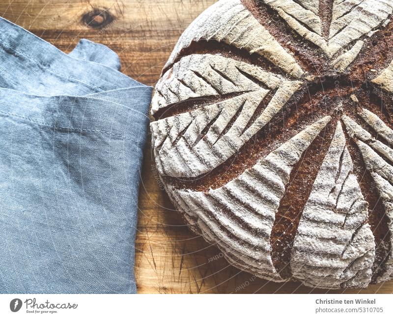A homemade bread with leaf pattern lies on a wooden board next to a blue linen cloth Bread Bread pattern Crust Crisp Bread love naturally Tradition Rustic Fresh