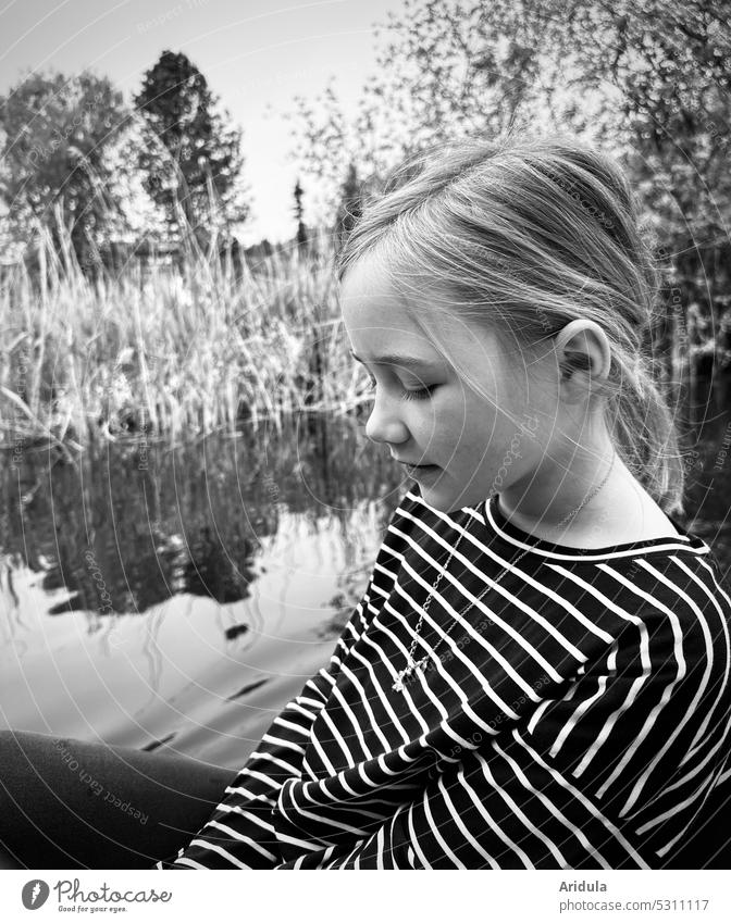 Girl sits in pedal boat on a lake and looks down. In the background: lake and shore b/w Child portrait Lake Water Lakeside bank Pedalo Waves Looking Trip