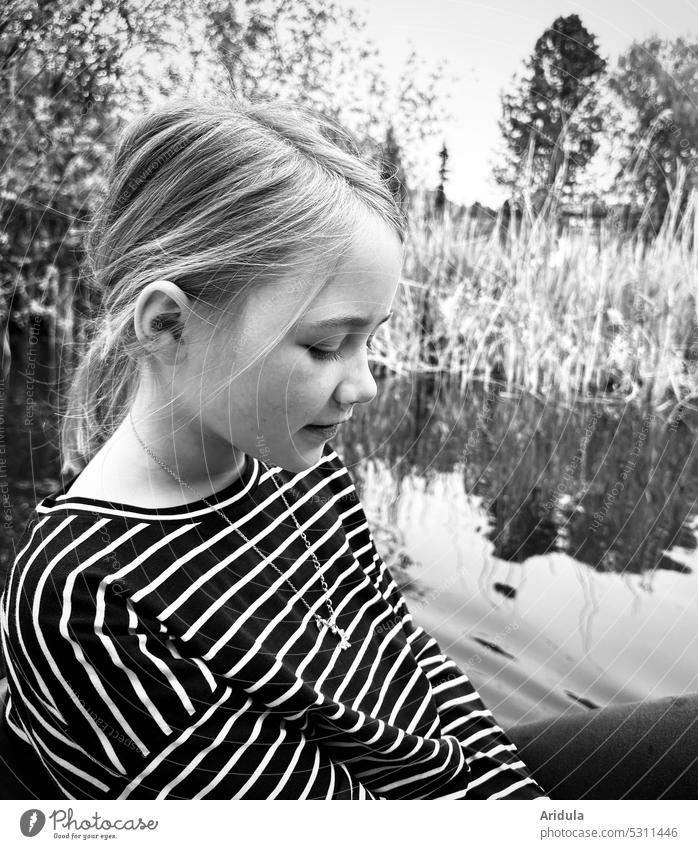 Girl sitting in boat with lake and shore in background looking down b/w Lake Pedalo Child Water bank Head striped shirt Leisure and hobbies Trip Exterior shot