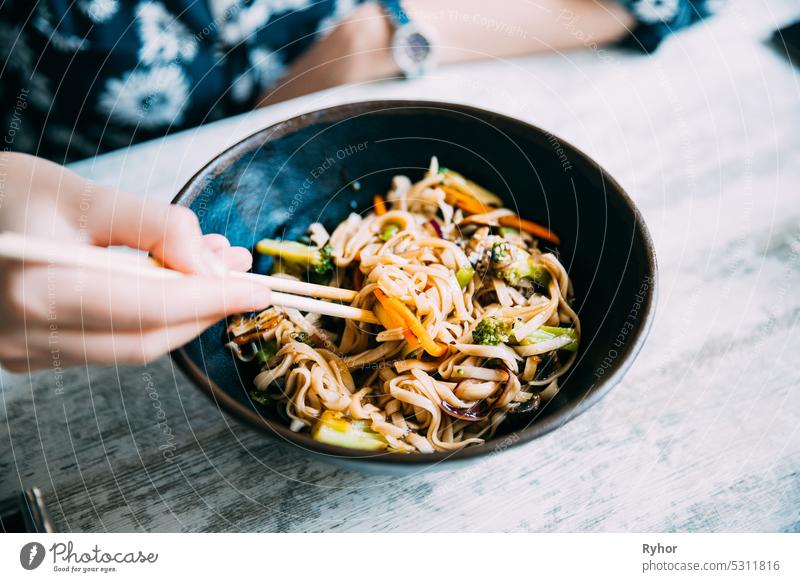 Woman eating asian noodles udon with pork in cafe. Asian noodles udon with pork close-up in a bowl on the table black chili chinese chopsticks closeup cooked