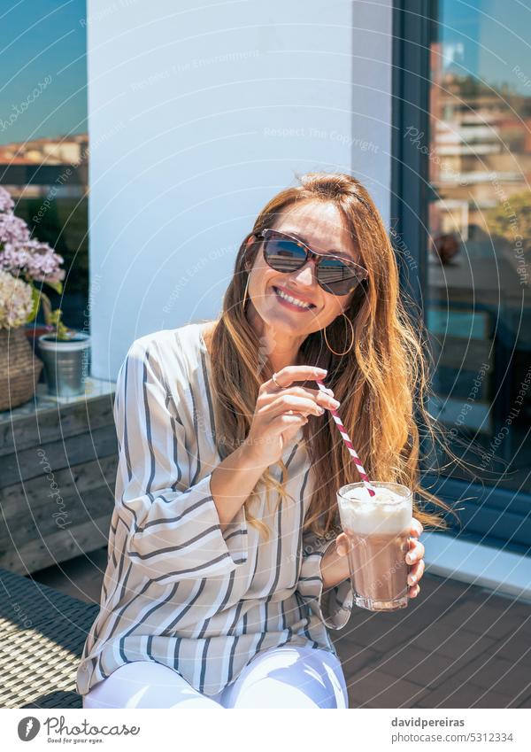 Smiling woman with sunglasses having a milkshake in rooftop portrait female smiling smile happy elegant terrace drinking attractive stylish cafeteria