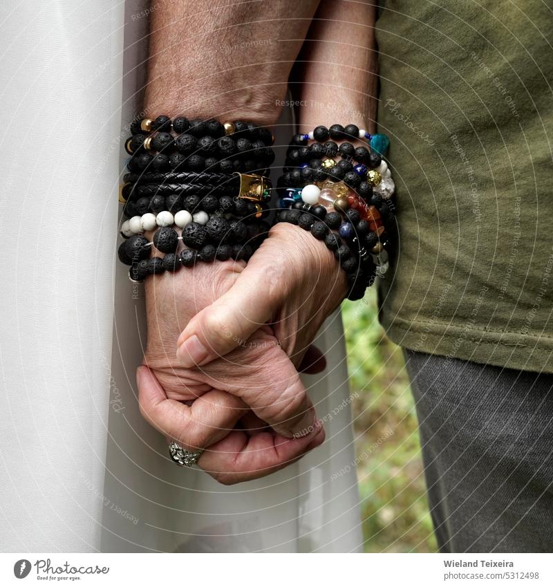 Elderly man and woman hold hands. They wear bracelets made of lava stone and other materials. person Stone White naturally Outdoors aged Old Close-up people