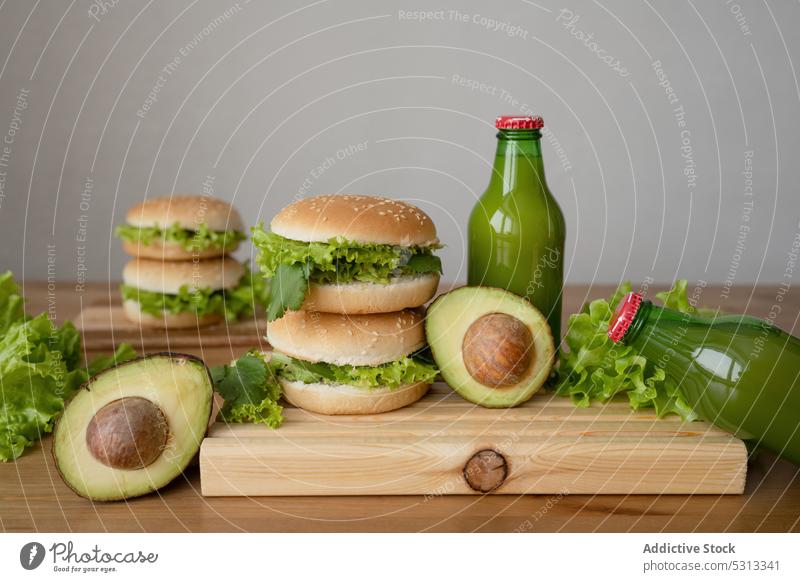 Delicious burger with vegetables and avocado on wooden board hamburger lettuce fresh vegetarian delicious cutting board bottle juice yummy food bun lunch