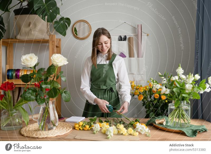Happy female florist pruning flowers at table woman cut bouquet shop positive work smile floral job plant bloom occupation apron professional blossom workplace