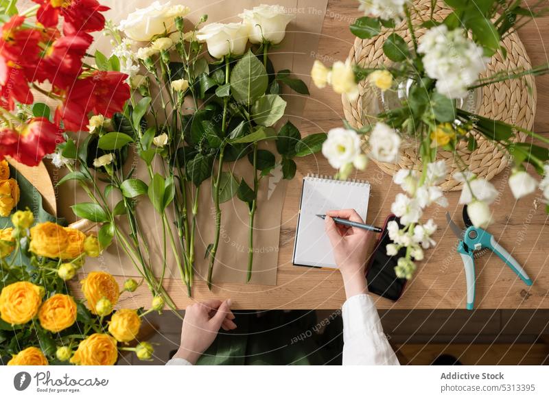 Crop florist taking notes in notebook woman take note work floristry blossom floral write bouquet workplace flower bloom store female table workspace job shop