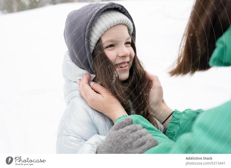 Anonymous mother with daughter having fun in snowy nature woman girl embrace adjust hug winter childcare park cap kid warm clothes cold childhood glove female