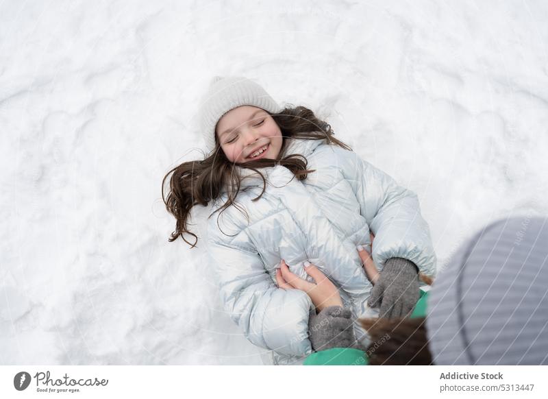 Cheerful girl in warm clothes lying on snow woman child tickle winter fun mother love daughter happy smile cheerful together season park nature cold positive