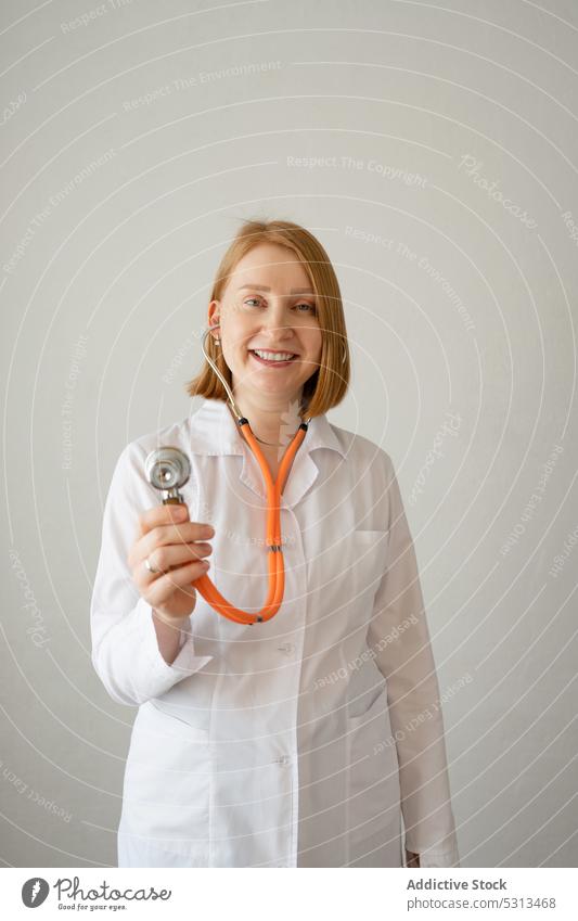 Cheerful woman standing with stethoscope in studio doctor uniform listen smile professional medic specialist physician female medical medicine clinic happy robe