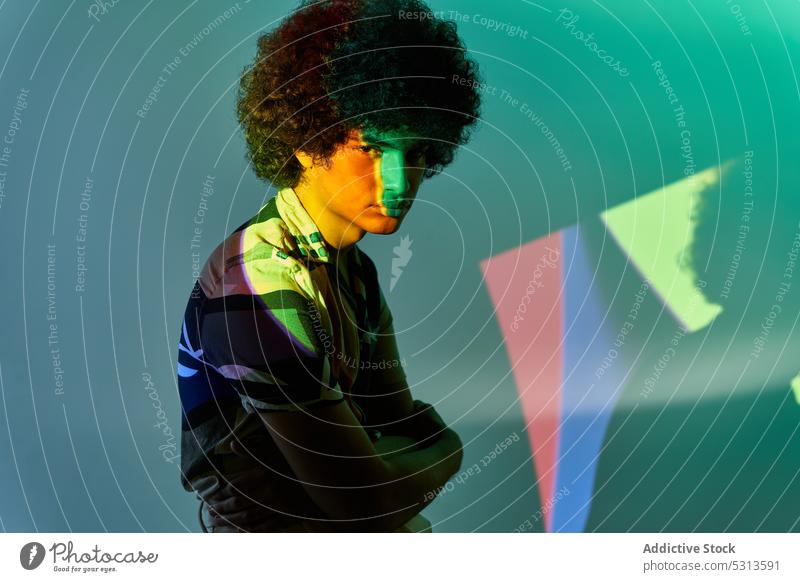 Hispanic guy sitting against colorful illumination looking at camera man model multicolored afro hair illuminate projector glow creative studio shot young male