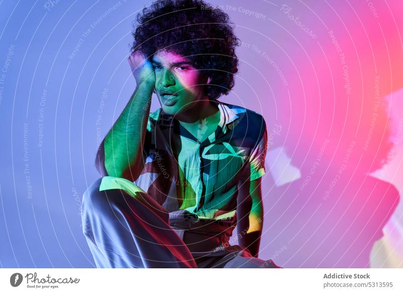 Hispanic guy leaning on hand sitting against colorful illumination with opened mouth man model multicolored lean on hand illuminate projector glow creative