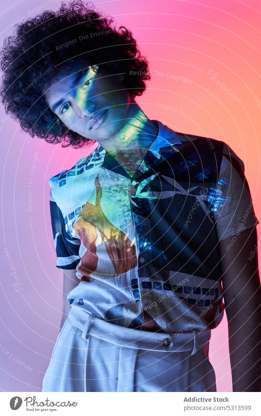 Hispanic guy leaning on hand sitting against colorful illumination looking at camera man model multicolored afro hair illuminate projector glow creative