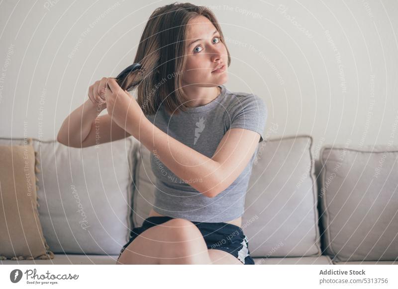 Dreamy woman brushing hair on sofa domestic calm comfort tranquil peaceful living room home young female style serene appearance couch thoughtful apartment