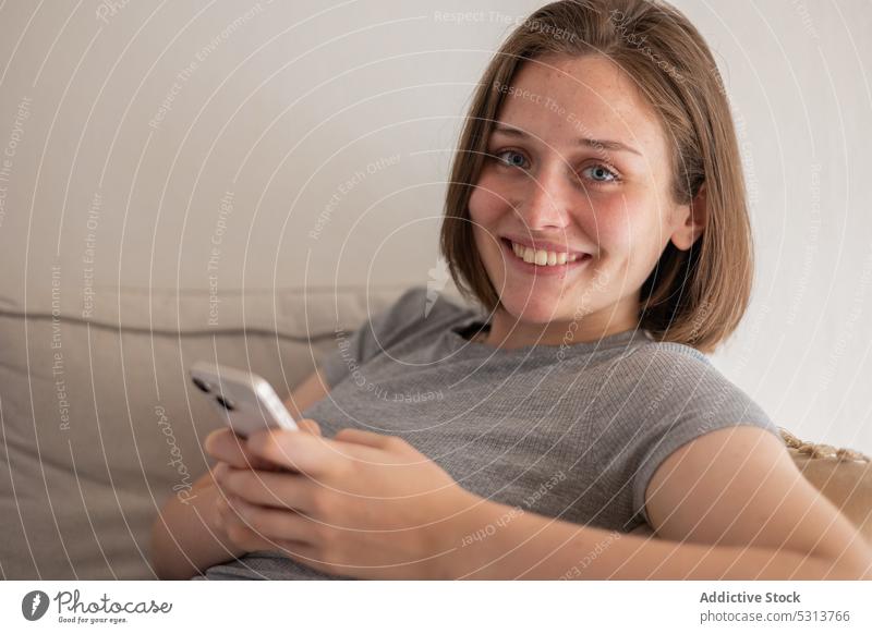 Content woman messaging via smartphone while sitting on sofa using home browsing domestic rest chill gadget couch device female living room mobile internet
