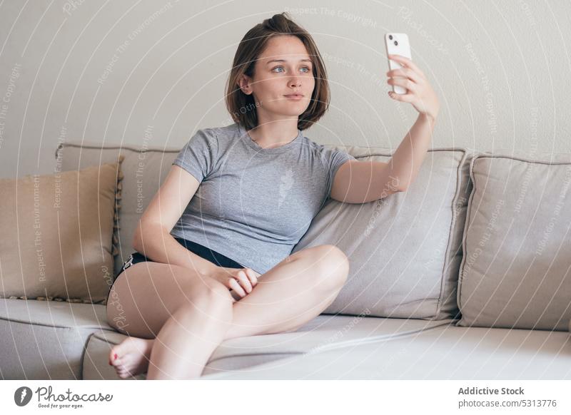 Charming woman taking selfie on smartphone on sofa chill home self portrait weekend rest using couch comfort female living room cozy gadget device calm mobile